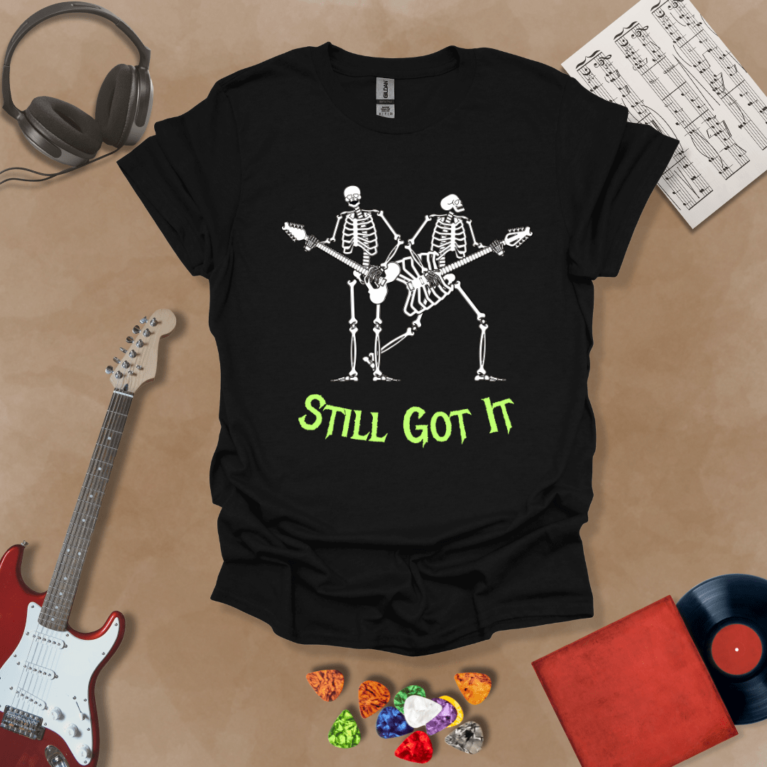 Black Vintage style t-shirt with Two skeletons playing guitars, text 'Still Got It' with bold retro lettering and rock vibe on a transparent background.