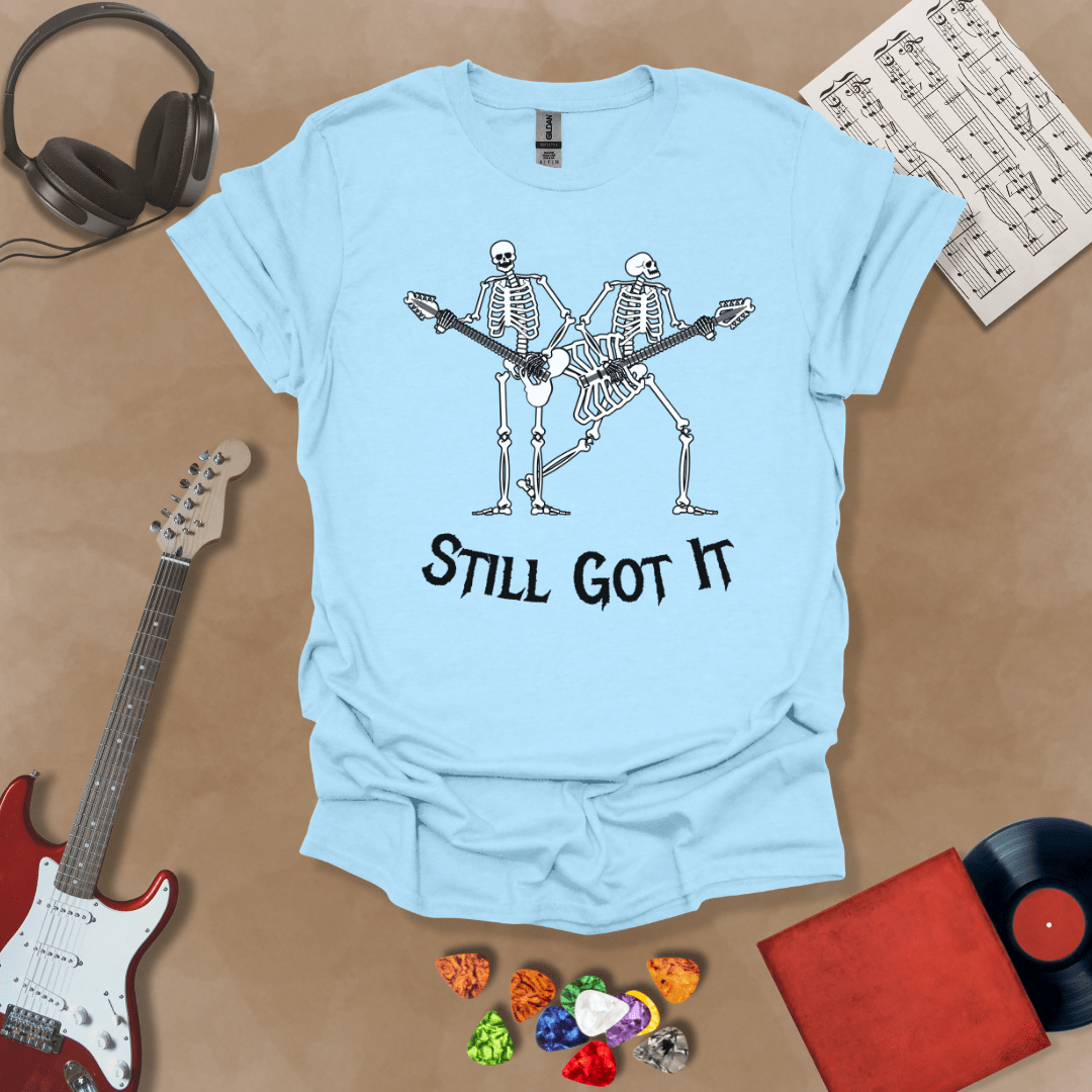 Light blue Vintage style t-shirt with Two skeletons playing guitars, text 'Still Got It' with bold retro lettering and rock vibe on a transparent background.