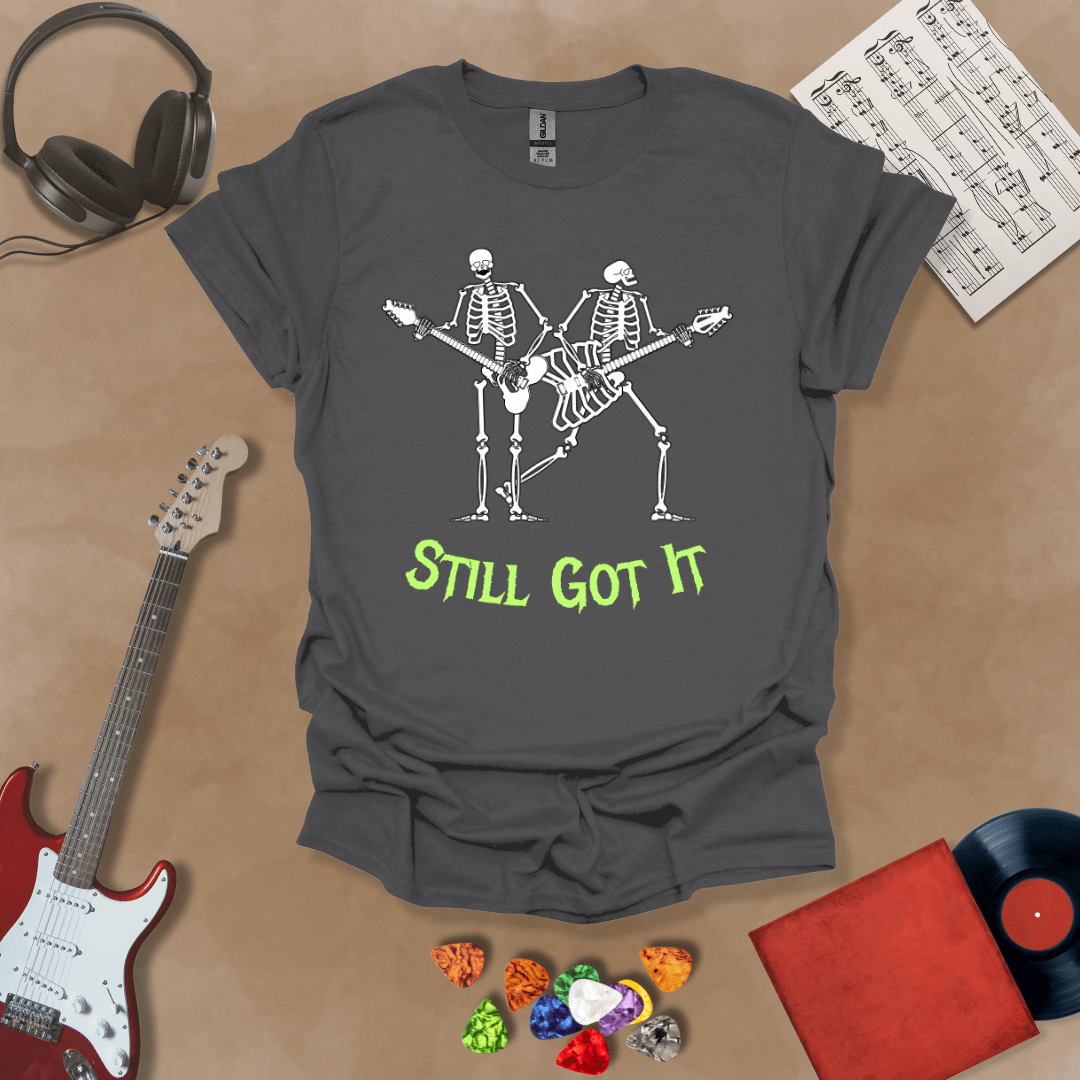 Gray Vintage style t-shirt with Two skeletons playing guitars, text 'Still Got It' with bold retro lettering and rock vibe on a transparent background.