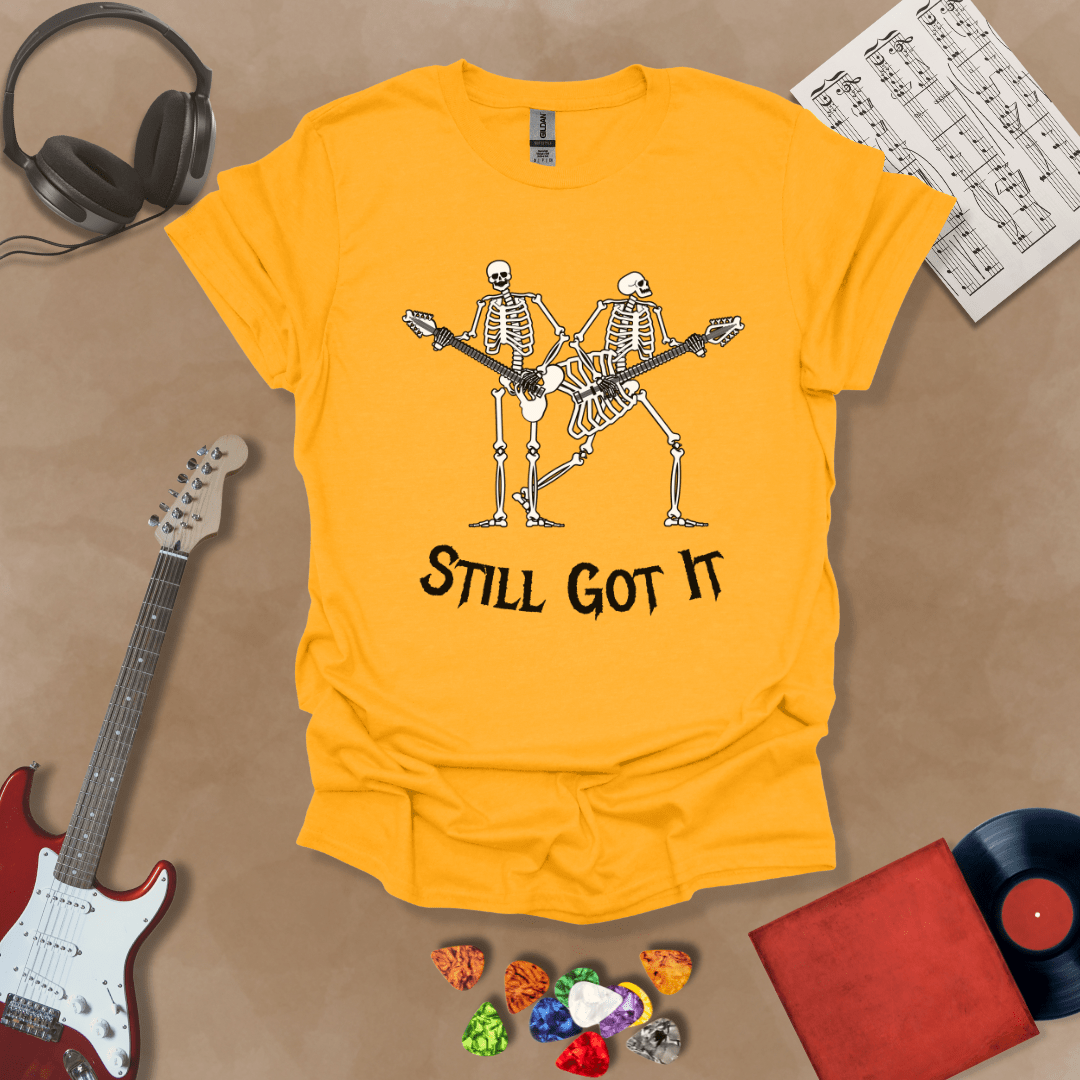 Yellow Vintage style t-shirt with Two skeletons playing guitars, text 'Still Got It' with bold retro lettering and rock vibe on a transparent background.