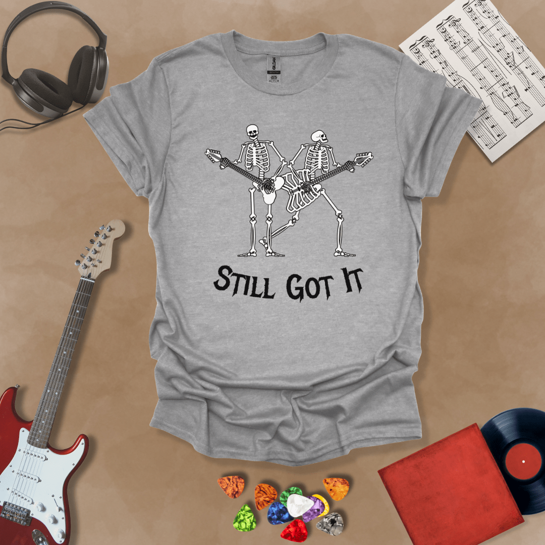 Gray Vintage style t-shirt with Two skeletons playing guitars, text 'Still Got It' with bold retro lettering and rock vibe on a transparent background.