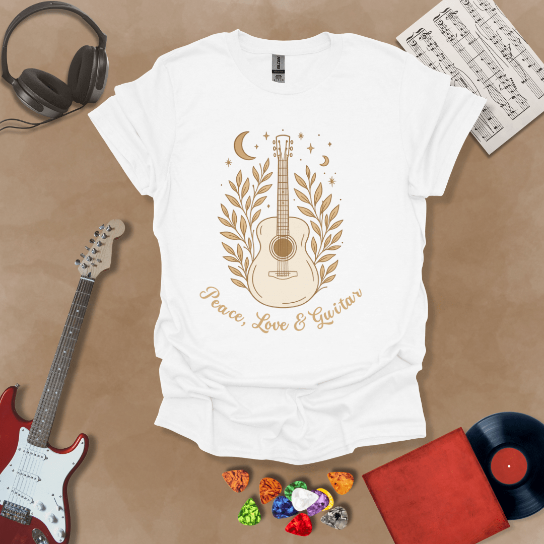 White t-shirt featuring an acoustic guitar surrounded by leaves, moons, and stars in an earthy, bohemian line-art style, with the text “Peace, Love & Guitar” below.
