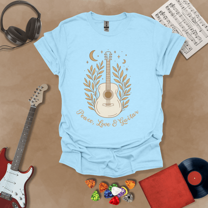 Light blue t-shirt featuring an acoustic guitar surrounded by leaves, moons, and stars in an earthy, bohemian line-art style, with the text “Peace, Love & Guitar” below.
