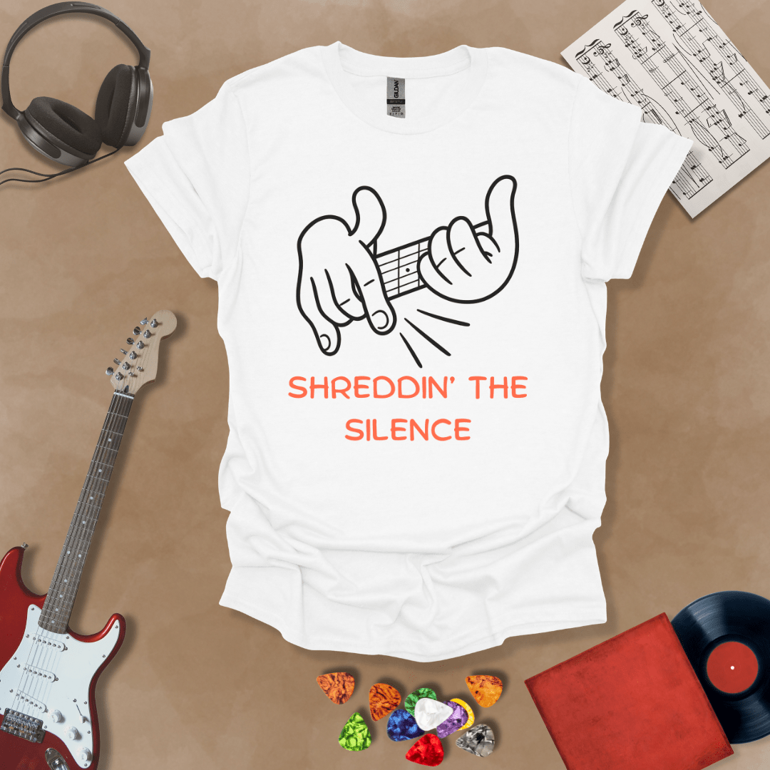 white  t-shirt featuring cartoon-style hands shredding a guitar riff with the text “Shreddin’ the Silence” in bold orange letters.
