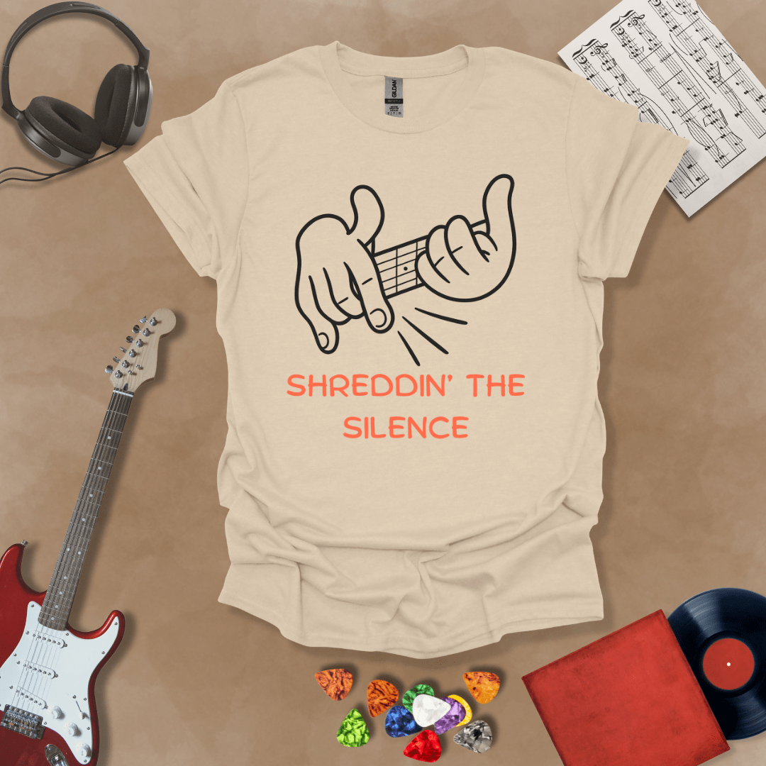 Beige t-shirt featuring cartoon-style hands shredding a guitar riff with the text “Shreddin’ the Silence” in bold orange letters.
