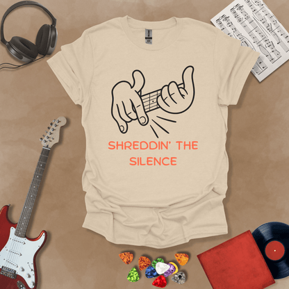Beige t-shirt featuring cartoon-style hands shredding a guitar riff with the text “Shreddin’ the Silence” in bold orange letters.
