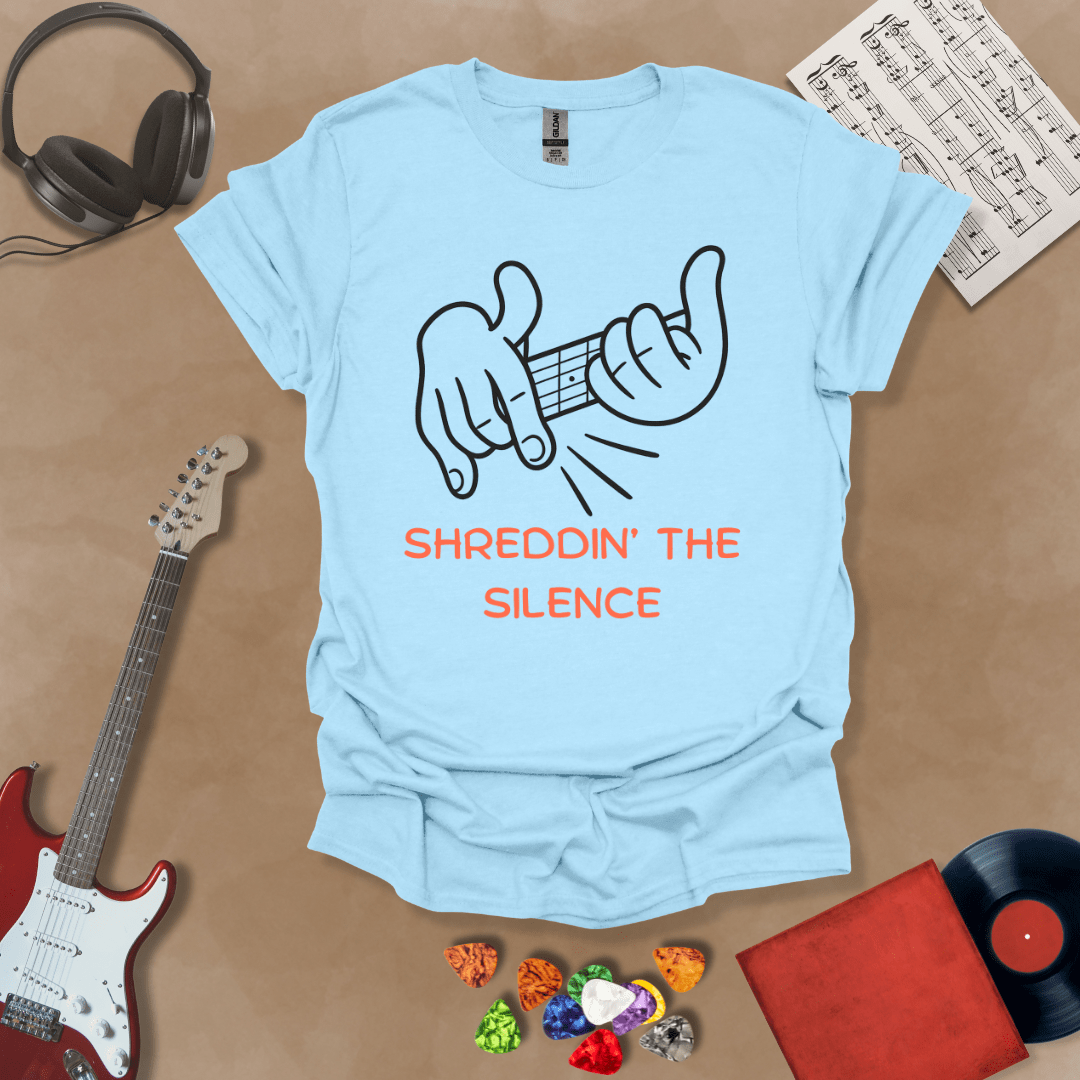 Light blue t-shirt featuring cartoon-style hands shredding a guitar riff with the text “Shreddin’ the Silence” in bold orange letters.
