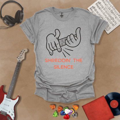 Gray t-shirt featuring cartoon-style hands shredding a guitar riff with the text “Shreddin’ the Silence” in bold orange letters.
