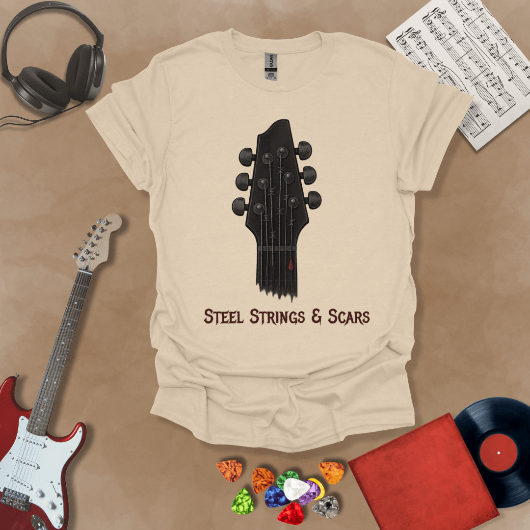 Beige t-shirt featuring a guitar headstock with razor-wire steel strings and a drop of blood, with the text “Steel Strings & Scars” below.
