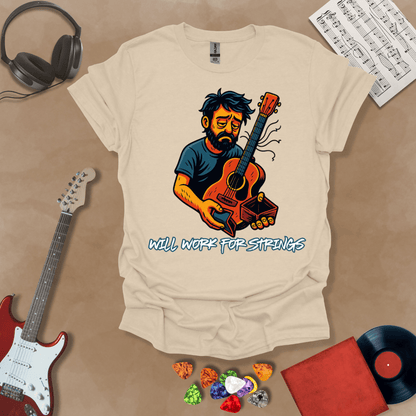 Beige t-shirt with a graphic of Cartoon-style illustration of a scruffy man holding a broken guitar and an empty wallet, looking sad. and text 'Will work for strings' .