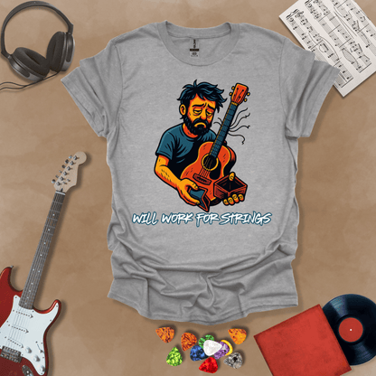 Gray  t-shirt with a graphic of Cartoon-style illustration of a scruffy man holding a broken guitar and an empty wallet, looking sad. and text 'Will work for strings' .