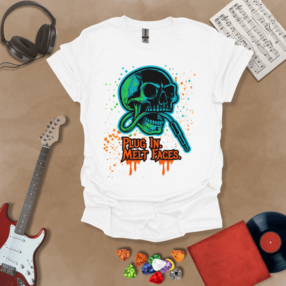 White t-shirt with neon-colored skull biting a guitar cable, paint splatter effect, text “Plug In. Melt Faces.”