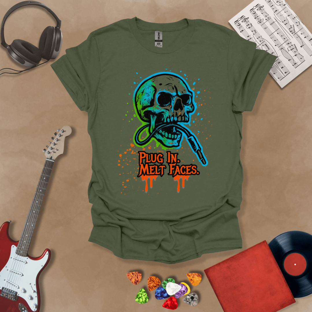 Green t-shirt with neon-colored skull biting a guitar cable, paint splatter effect, text “Plug In. Melt Faces.”