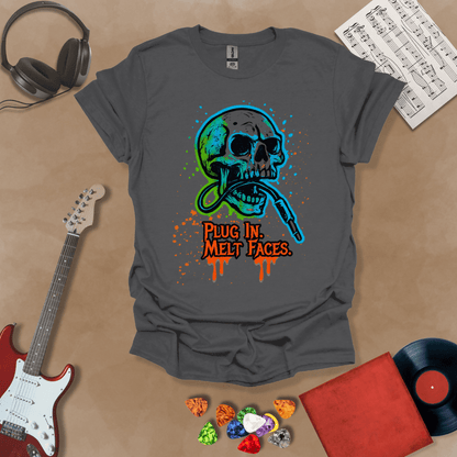 Gray t-shirt with neon-colored skull biting a guitar cable, paint splatter effect, text “Plug In. Melt Faces.”