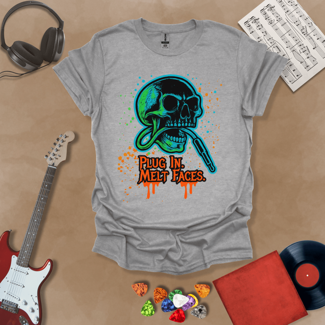 Gray t-shirt with neon-colored skull biting a guitar cable, paint splatter effect, text “Plug In. Melt Faces.”