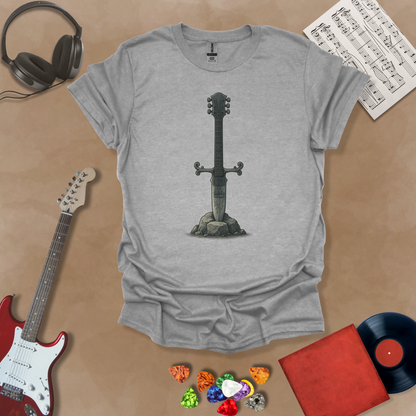 Gray T-shirt with detailed illustration of a stone-forged guitar sword glowing in silver tones, titled Axecalibur: Blade of Light, printed on a light tee by Riff Junkie.