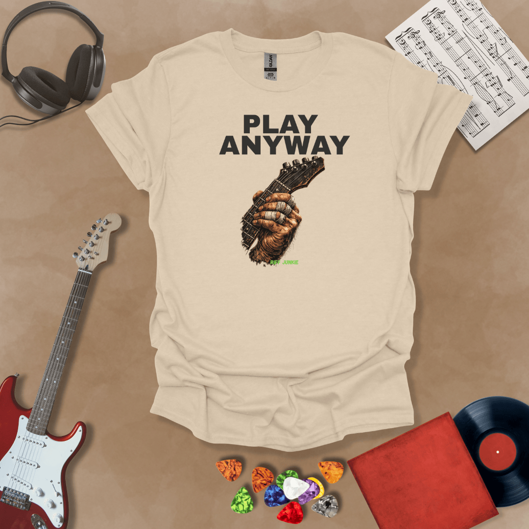 Play Anyway – Riff Edition graphic Beige t-shirt featuring bold stacked text above a weathered hand gripping a guitar fretboard with taped fingers and Riff Junkie branding.