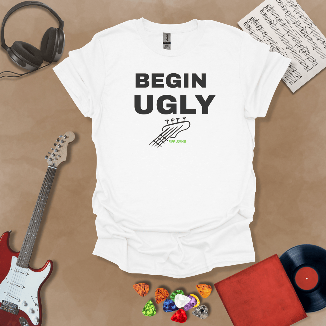 Begin Ugly – Jax Edition white graphic t-shirt featuring bold stacked text with distressed guitar headstock accent and subtle Riff Junkie branding. Motivational creator apparel design.