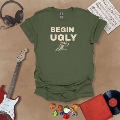 Begin Ugly – Jax Edition green graphic t-shirt featuring bold stacked text with distressed guitar headstock accent and subtle Riff Junkie branding. Motivational creator apparel design.