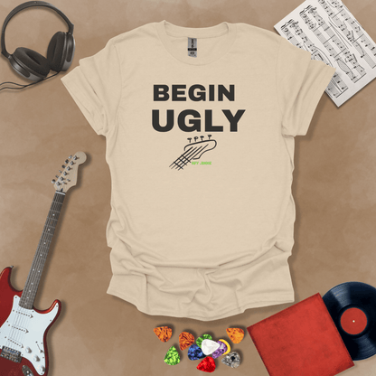 Begin Ugly – Jax Edition beige graphic t-shirt featuring bold stacked text with distressed guitar headstock accent and subtle Riff Junkie branding. Motivational creator apparel design.