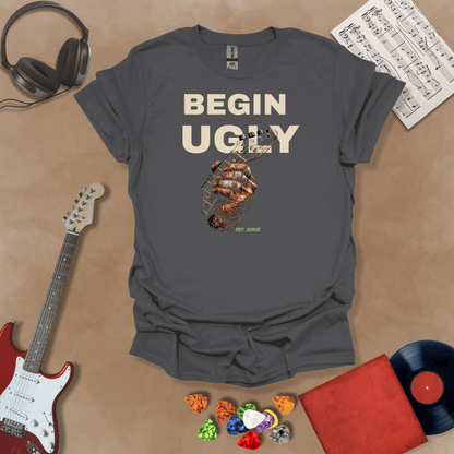 Begin Ugly – Riff Edition gray graphic t-shirt featuring bold stacked text above a weathered hand gripping a guitar fretboard with taped fingers and subtle Riff Junkie branding.