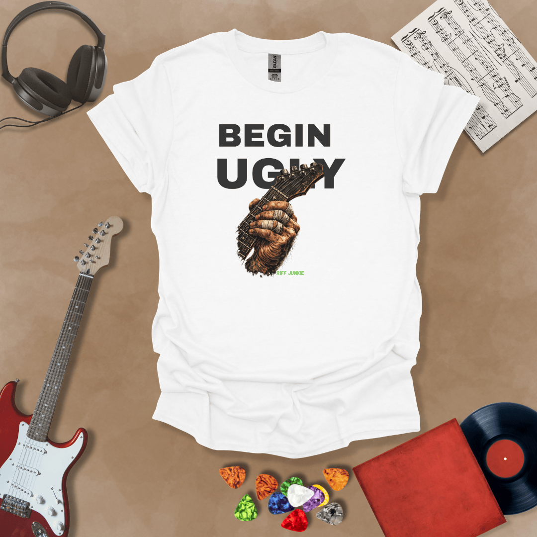 Begin Ugly – Riff Edition white graphic t-shirt featuring bold stacked text above a weathered hand gripping a guitar fretboard with taped fingers and subtle Riff Junkie branding.