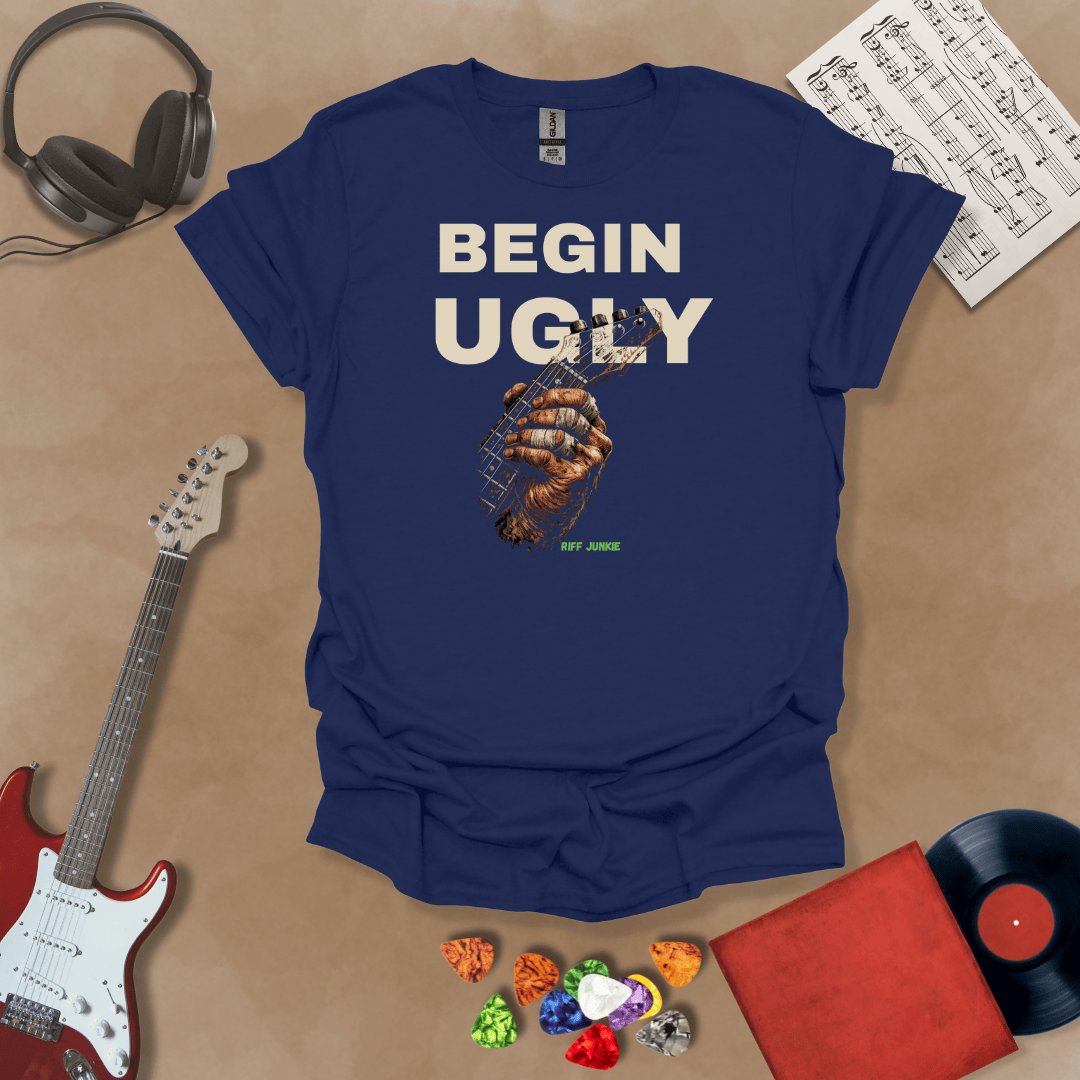Begin Ugly – Riff Edition navy graphic t-shirt featuring bold stacked text above a weathered hand gripping a guitar fretboard with taped fingers and subtle Riff Junkie branding.