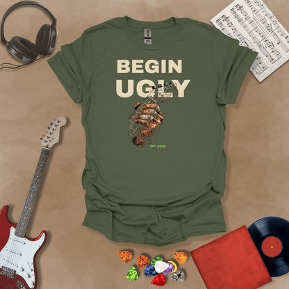 Begin Ugly – Riff Edition green graphic t-shirt featuring bold stacked text above a weathered hand gripping a guitar fretboard with taped fingers and subtle Riff Junkie branding.