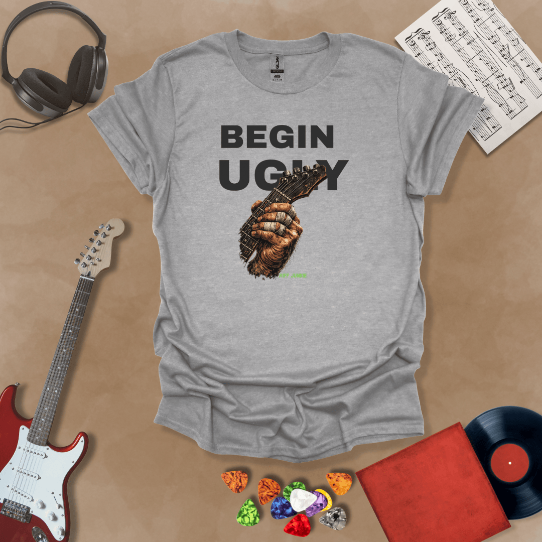 Begin Ugly – Riff Edition gray graphic t-shirt featuring bold stacked text above a weathered hand gripping a guitar fretboard with taped fingers and subtle Riff Junkie branding.