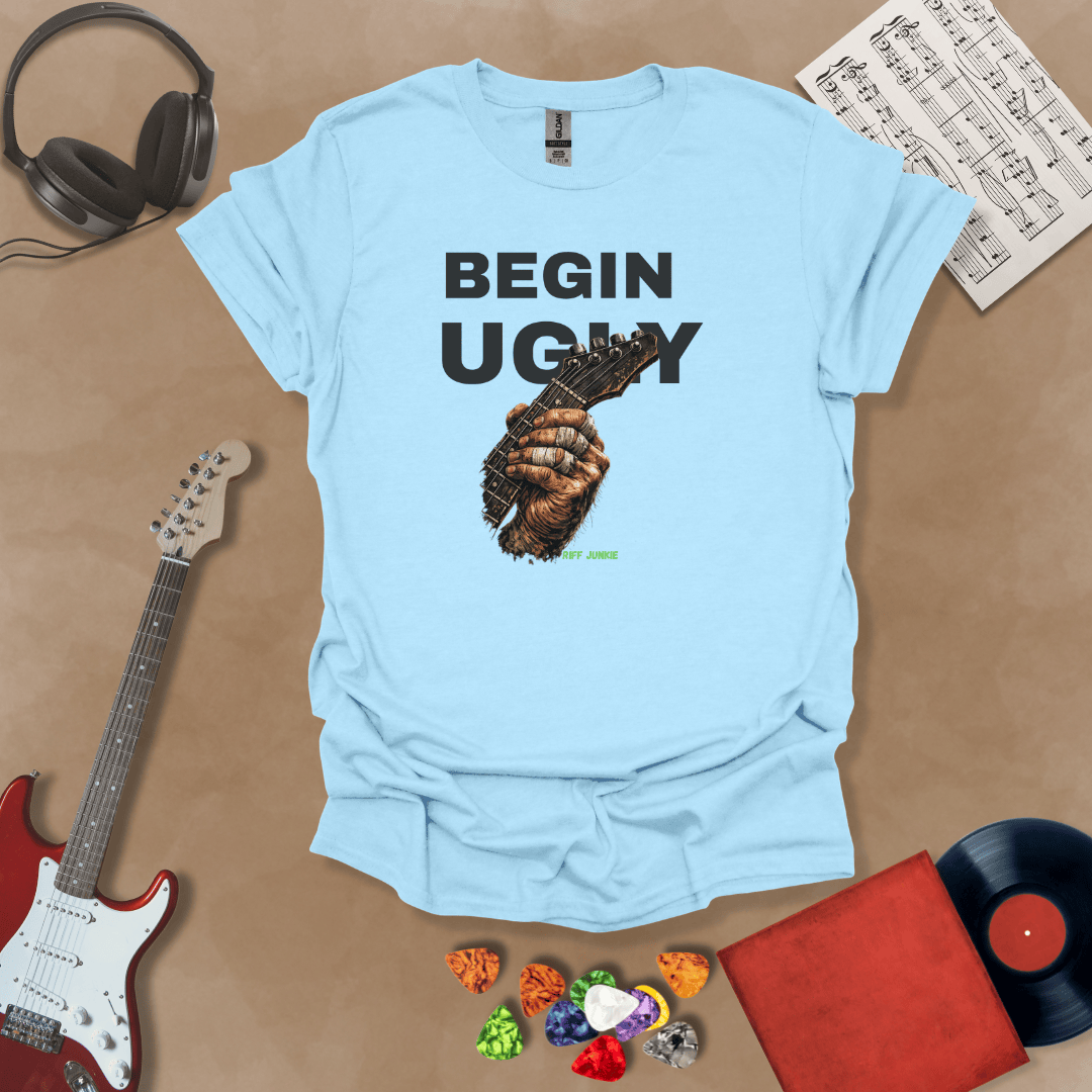 Begin Ugly – Riff Edition blue graphic t-shirt featuring bold stacked text above a weathered hand gripping a guitar fretboard with taped fingers and subtle Riff Junkie branding.
