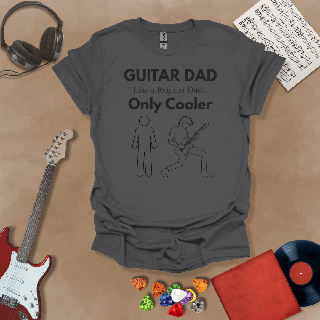 A dark gray Guitar Dad Sketch Edition t-shirt featuring a hand-drawn illustration of a regular dad and a rocker dad, laid flat on a tan background with guitar-themed props.