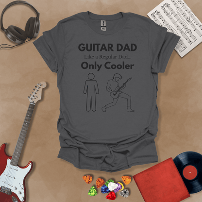 A dark gray Guitar Dad Sketch Edition t-shirt featuring a hand-drawn illustration of a regular dad and a rocker dad, laid flat on a tan background with guitar-themed props.