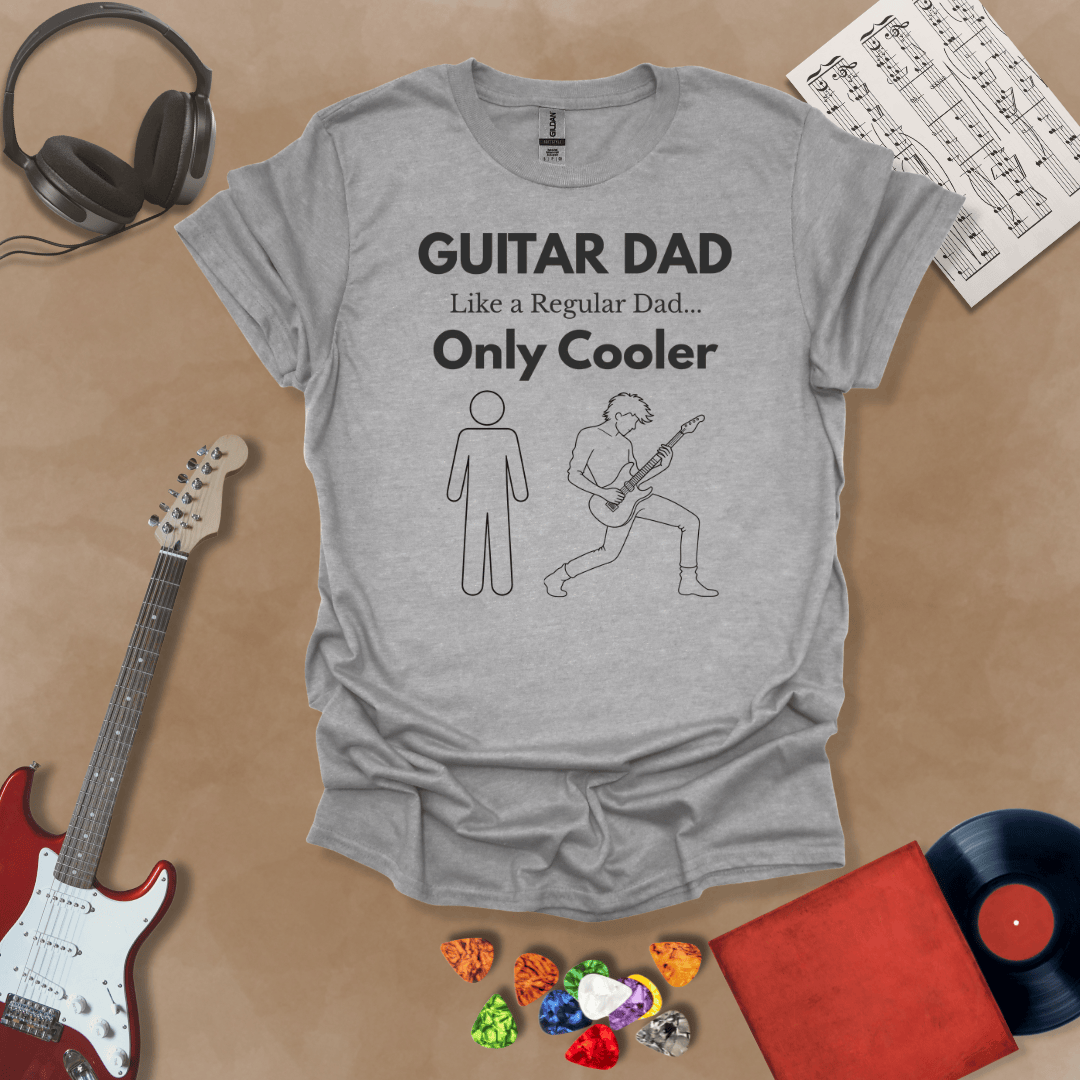 A light gray Guitar Dad Sketch Edition t-shirt featuring a hand-drawn illustration of a regular dad and a rocker dad, laid flat on a tan background with guitar-themed props.