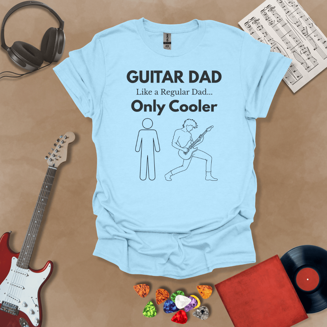 A light blue Guitar Dad Sketch Edition t-shirt featuring a hand-drawn illustration of a regular dad and a rocker dad, laid flat on a tan background with guitar-themed props.