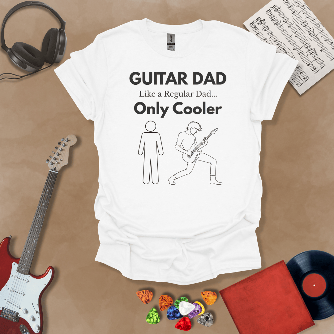 A white Guitar Dad Sketch Edition t-shirt featuring a hand-drawn illustration of a regular dad and a rocker dad, laid flat on a tan background with guitar-themed props.