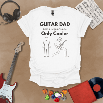 A white Guitar Dad Sketch Edition t-shirt featuring a hand-drawn illustration of a regular dad and a rocker dad, laid flat on a tan background with guitar-themed props.
