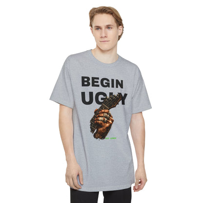 A man wearing a gray short-sleeve t-shirt featuring a graphic print on the front. The design displays the text 'BEGIN UGLY' in a distressed cream-colored font above an illustration of a hand holding a guitar, with  "Riff Junkie" in neon green.