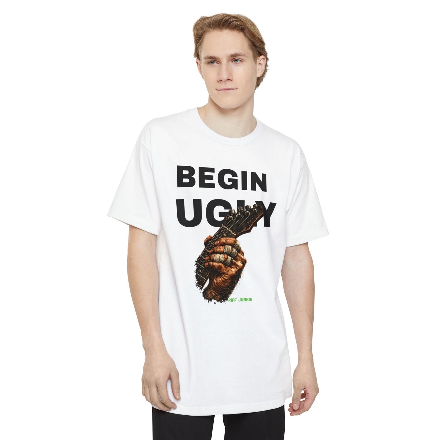 A man wearing a white short-sleeve t-shirt featuring a graphic print on the front. The design displays the text 'BEGIN UGLY' in a distressed cream-colored font above an illustration of a hand holding a guitar, with  "Riff Junkie" in neon green.